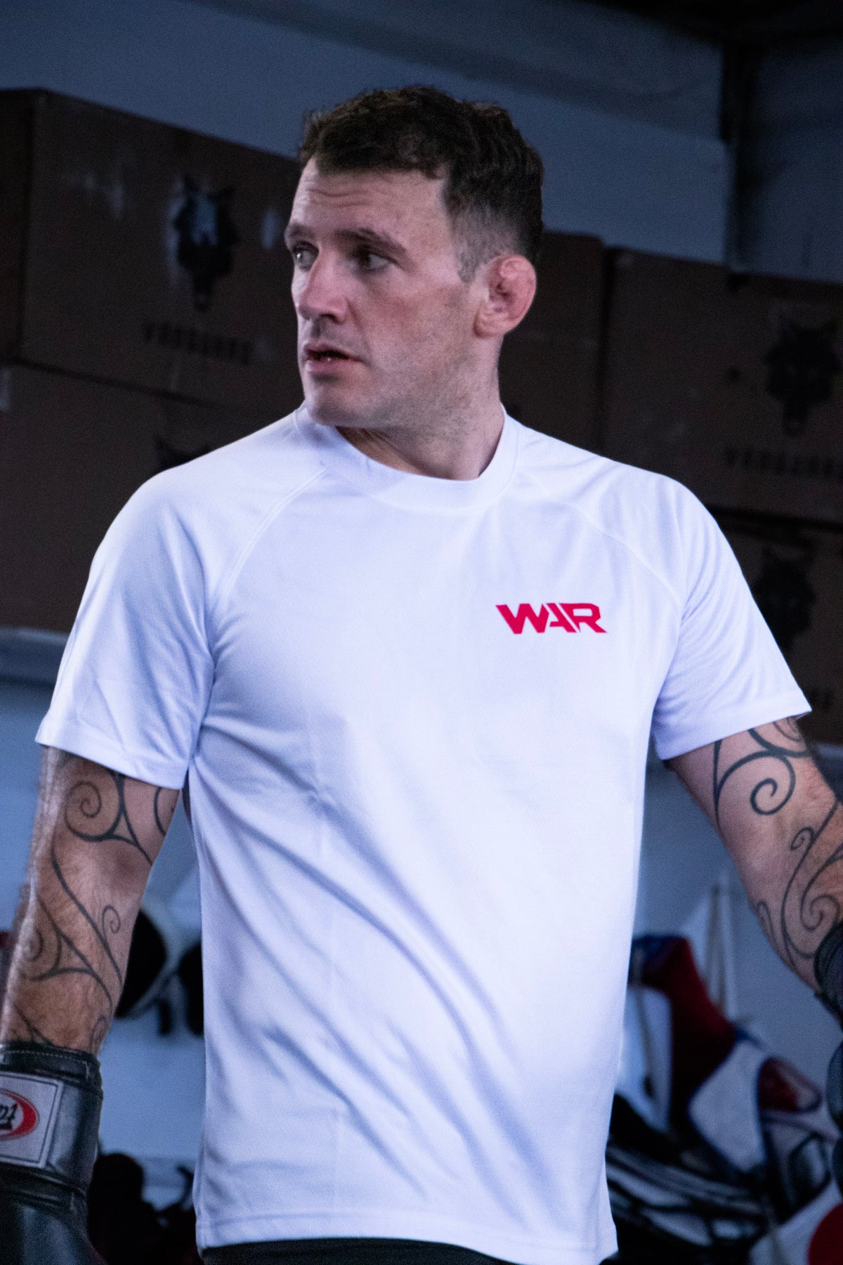 A man wearing a white athletic t-shirt with a red 'WAR' logo on the chest, standing in a gym environment.